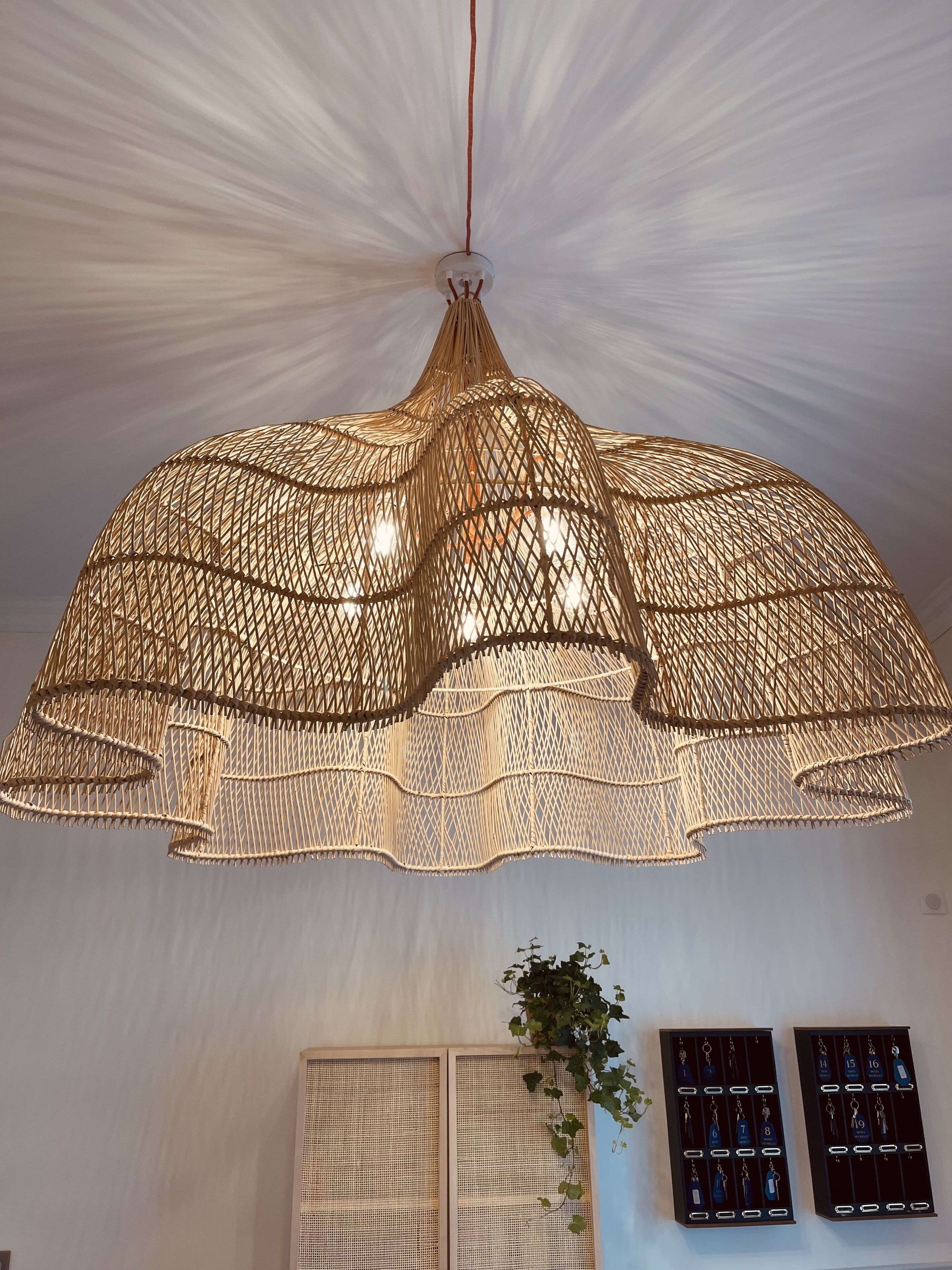 A large, woven pendant light fixture with a central bulb, hanging from a white ceiling.