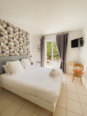 A hotel room with a large bed, a desk, a chair, a flat-screen TV, and a view of the outdoors. - Hôtel Michelet Plage (Soulac-sur-Mer)