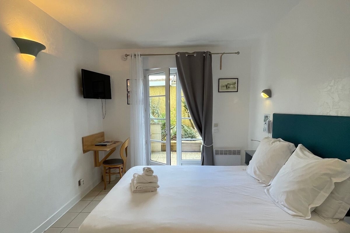 A hotel room with a bed, a desk, a chair, a television, and a window with curtains.