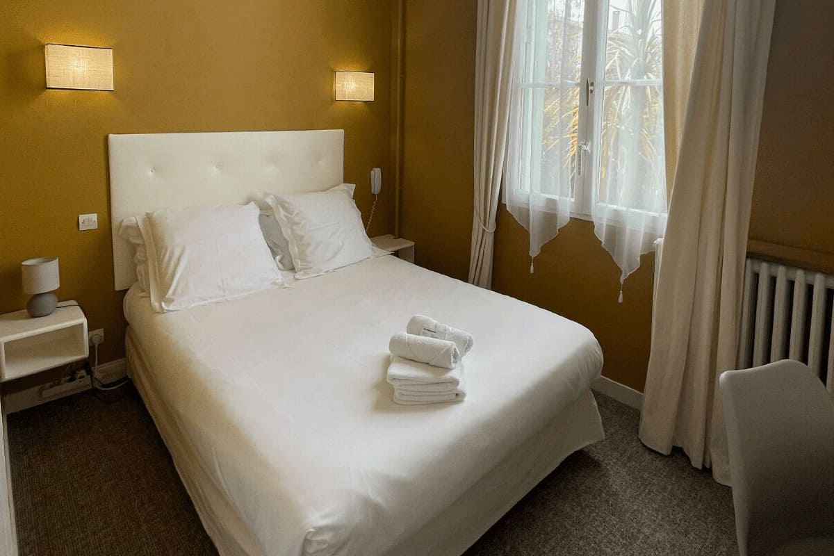 A neatly made bed with white linens and a folded towel, a bedside lamp, and a nightstand with a phone.