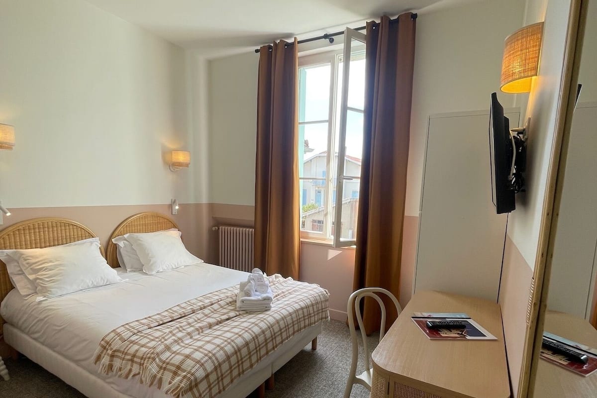 A hotel room with a bed, a desk, a chair, a television, and a window with curtains.