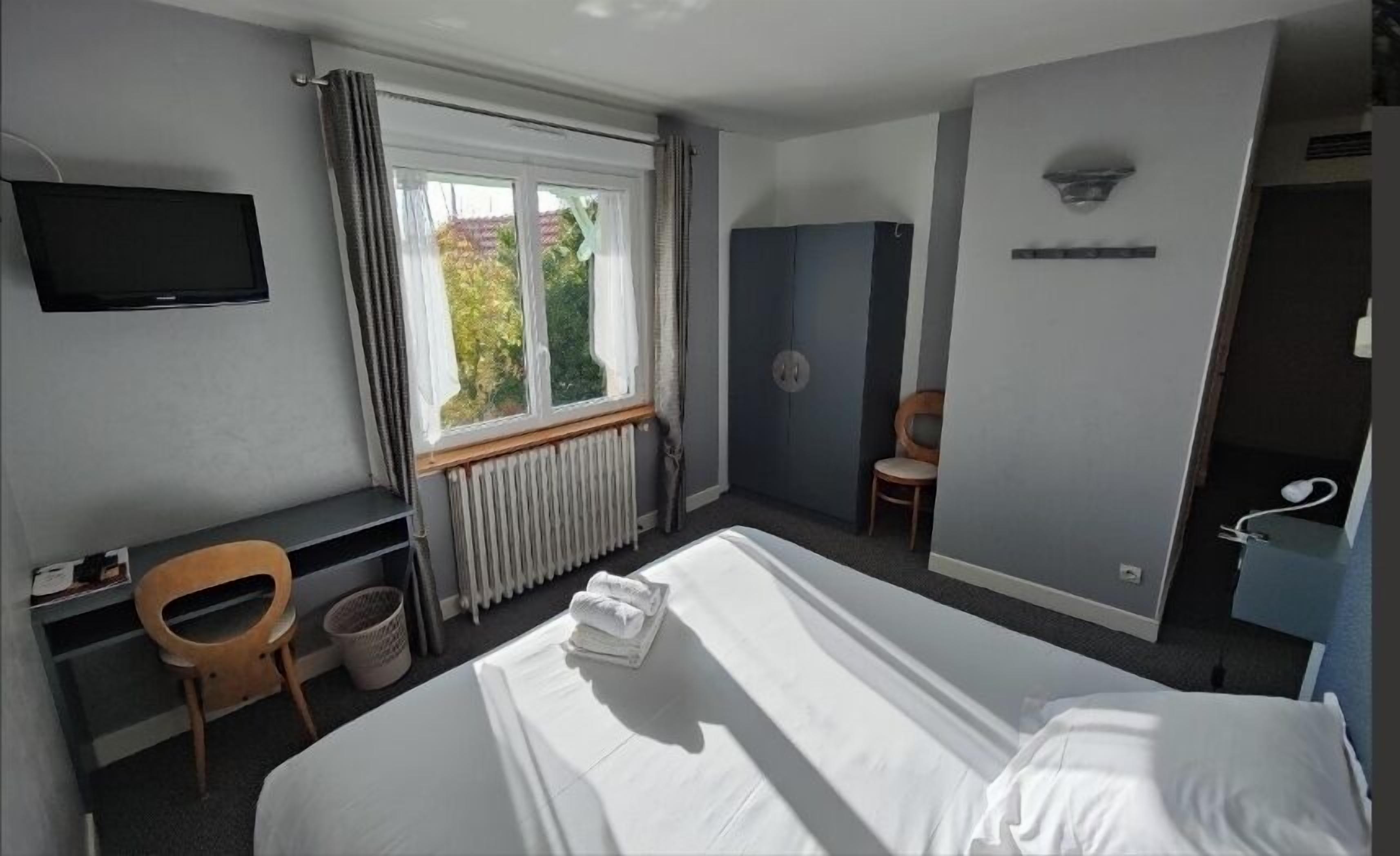 A hotel room with a bed, a desk, a chair, a television, and a window with curtains.