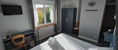A hotel room with a bed, a desk, a chair, a television, and a window with curtains.