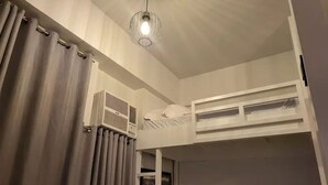 Ein Schlafsaalzimmer mit Stockbetten, einem Deckenventilator und einem Vorhangfenster.