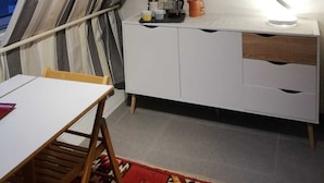Una habitación con un armario blanco, un cuadro de un toro, una ventana con cortinas y una mesa con una silla.