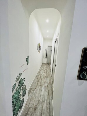 A narrow hallway with a wooden floor, white walls, and a door at the end.