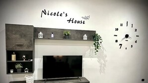 Ein modernes Wohnzimmer mit einem an der Wand befestigten Fernseher, einer Wanduhr und einem Regal mit Dekorationsobjekten.
