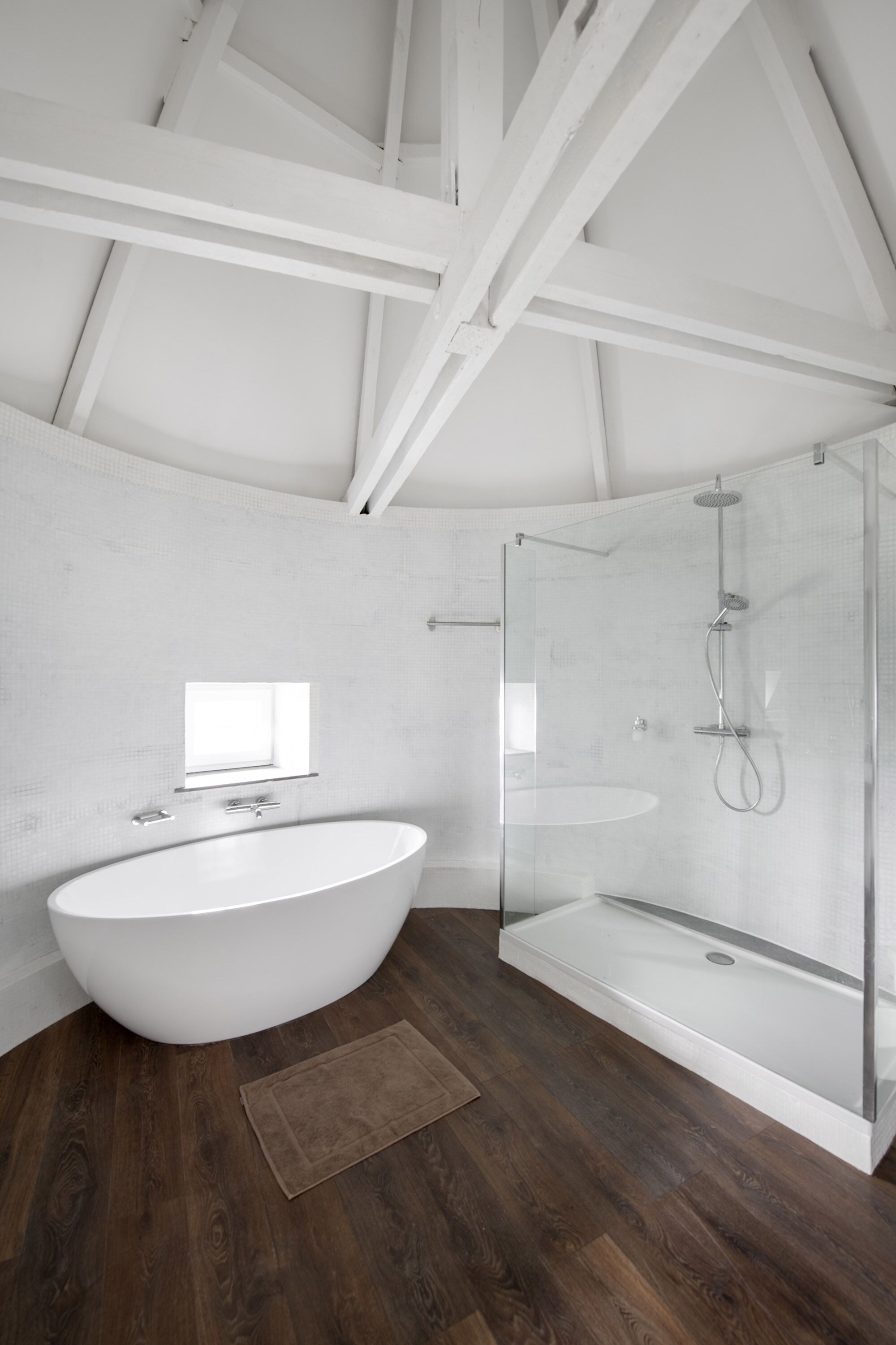 Une salle de bain moderne avec une baignoire sur pieds, une douche à parois de verre et une petite fenêtre.