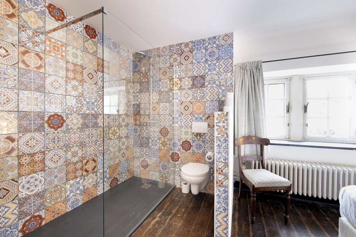 A bathroom with patterned tiles, a toilet, a shower, and a wooden chair.