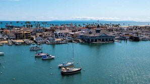 A marina with boats docked, a coastal town with buildings, and a clear view of the sea and mountains in the background.