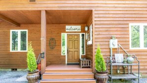 A wooden cabin with a 'welcome' sign, a door, steps leading to the entrance, and two potted plants. - Magical Private House in Forest w/Hot Tub. Near Wineries! (Woodinville)