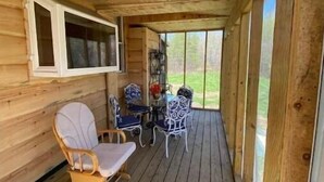 A wooden deck with a table and chairs, a window, and a view of the outdoors. - Forest Side Solar Powered Cabin with Nature Trails (Norfolk)