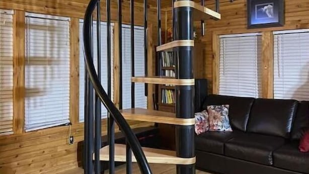 A wooden interior with a spiral staircase, a black leather sofa, and a fireplace. - Forest Side Solar Powered Cabin with Nature Trails (Norfolk)