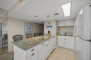 A kitchen with white cabinets, a granite countertop, and a white refrigerator. There is a star decoration on the wall and a framed picture above the counter.