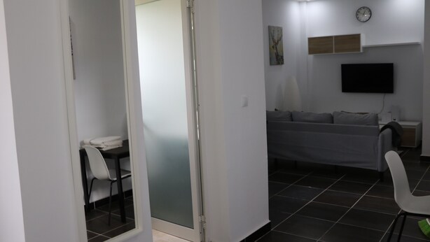 En moderne stue med en sofa, et fjernsyn ophængt på væggen og et spiseområde med stole og et bord.