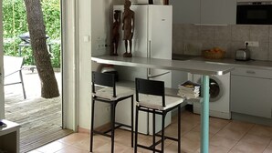 Uma cozinha compacta com máquina de lavar embutida, micro-ondas e torradeira. Há duas cadeiras e uma mesa pequena.