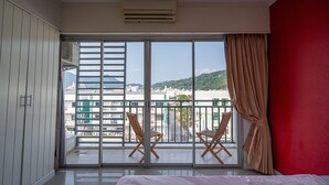 Hotellihuone, jossa on parveke, sänky ja kaksi puista tuolia.