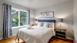 A bedroom with a large bed, a nightstand, a lamp, and a window with curtains.