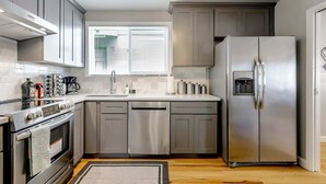 A modern kitchen with grey cabinets, stainless steel appliances, a built-in oven, and a refrigerator with a water dispenser.