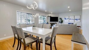 A modern dining area with a white table, four grey upholstered chairs, and a wooden floor.