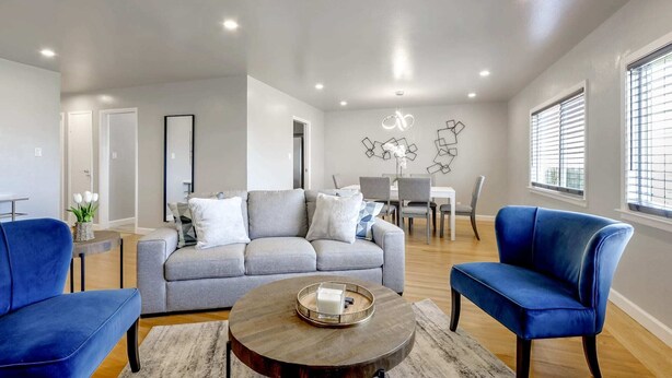 A modern living room with a grey sofa, blue armchairs, a coffee table, and a dining area with a white table and chairs.
