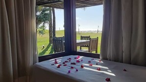 Een kamer met een bed, een tafel en uitzicht op een grasveld en palmbomen.