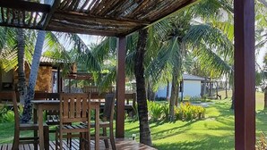 Een houten terras met een tafel en stoelen, omringd door palmbomen en een verzorgd gazon.