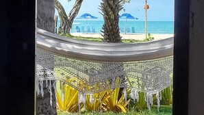 Een hangmat gespannen tussen bomen met uitzicht op een strand met parasols en een helder uitzicht over de oceaan.