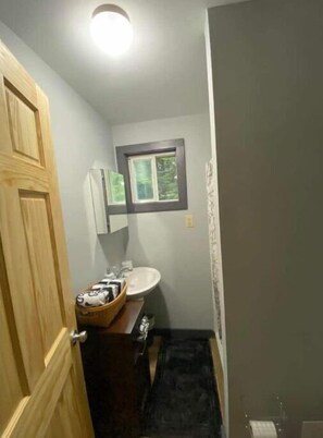A small bathroom with a wooden door, a sink, a mirror, and a window.