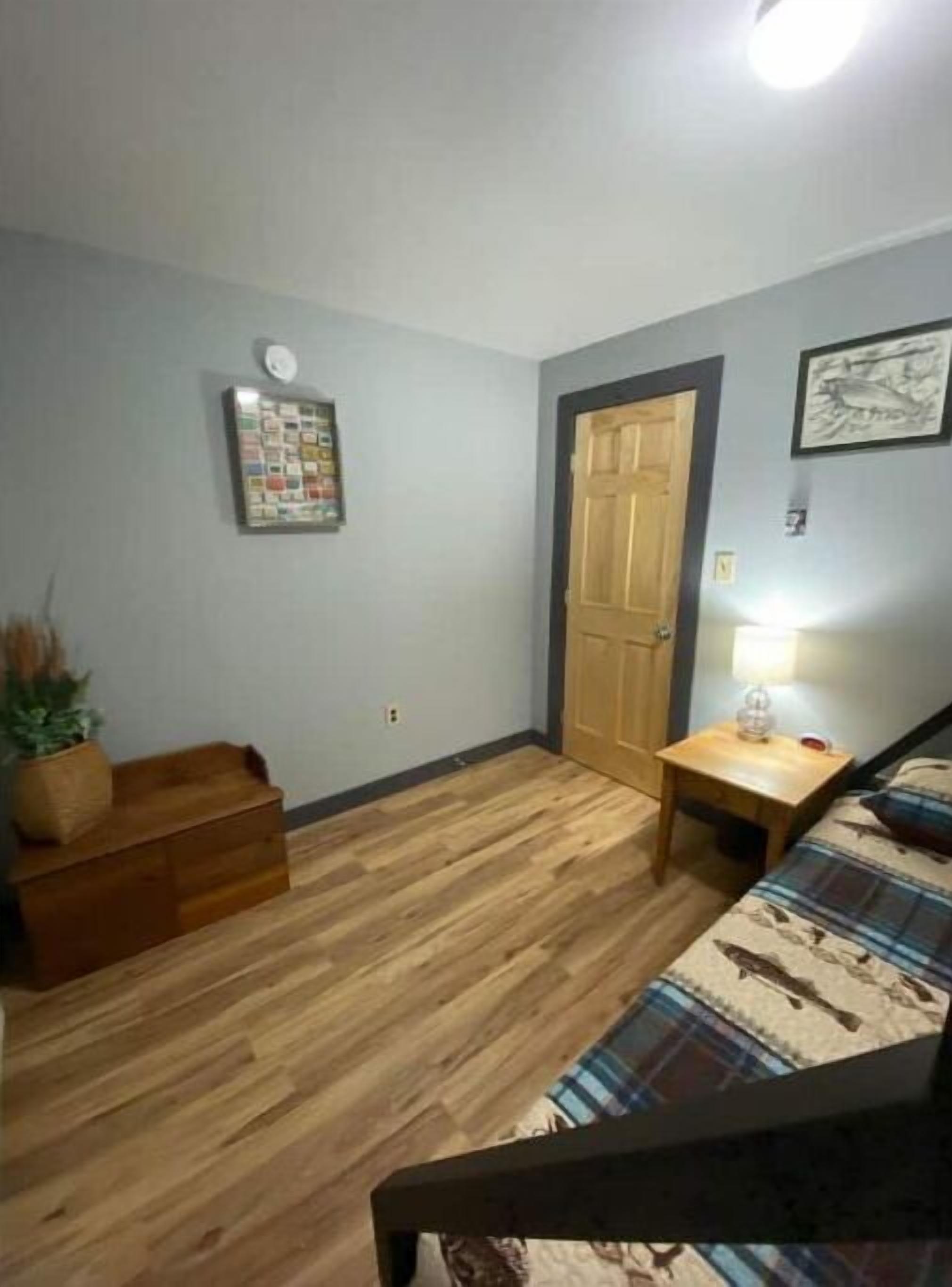 Una habitación pequeña y acogedora con un banco de madera, una mesita con una lámpara y una puerta.