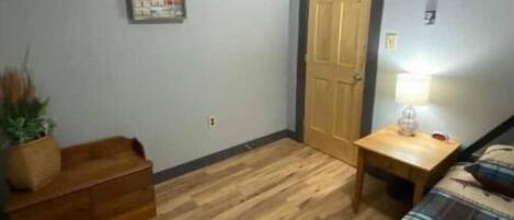 Una habitación pequeña y acogedora con un banco de madera, una mesita con una lámpara y una puerta.