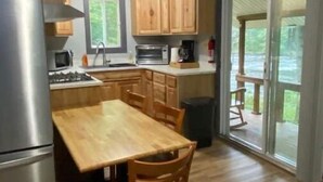 Een compacte keuken met houten kastjes, een roestvrijstalen koelkast, een magnetron en een kookplaat. Er is een eettafel met stoelen en uitzicht op een terras door glazen deuren.