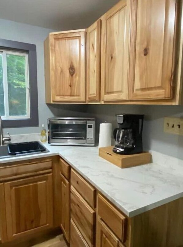 A kitchen with wooden cabinets, a microwave, a coffee maker, and a window. - Riverside cabin, fly-fish for trout or just relax! (Malone)