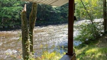 A wooden deck overlooking a river with trees and greenery in the background.