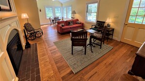 Un vaste salon doté de parquet, d’une cheminée, d’un canapé rouge et d’un coin repas avec une table et des chaises.