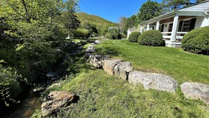 Une maison avec une pelouse bien entretenue, un muret en pierre et un petit ruisseau.