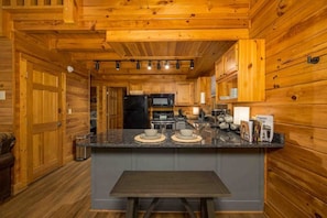 Kitchen features a central island, black refrigerator, microwave, and sink, with cabinets above the countertop.