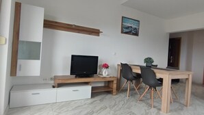 Un soggiorno moderno con TV, scrivania in legno, sedie e tavolo da pranzo.