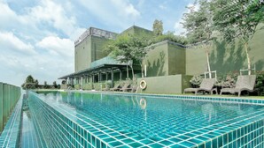 A swimming pool with a tiled edge, surrounded by lounge chairs and a building with a green facade. - Homey Family Gateway (Petaling Jaya)
