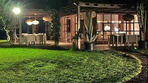 A well-lit outdoor dining area with tables and chairs, surrounded by potted plants and a grassy lawn. - Luxurious Villa Beldi Chic 20 minutes from Marrakech Medina (Tamesloht)