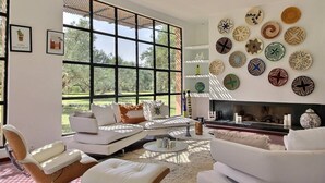 A modern living room with a large window, white furniture, and a wall decorated with various patterned plates. - Luxurious Villa Beldi Chic 20 minutes from Marrakech Medina (Tamesloht)