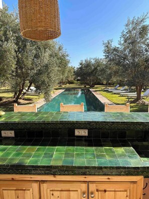Zona de piscina con terraza de baldosas verdes, sillas de descanso y olivos.