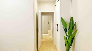 A narrow hallway with wooden flooring, white walls, and a door leading to another room.
