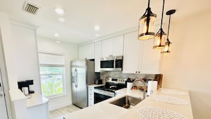 A modern kitchen with white cabinetry, stainless steel appliances, and a central island with a sink and a microwave. - Waterfront Condo, 8 min drive to Marco Beaches (Naples)