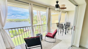 A balcony with a view of a lake, a ceiling fan, and a table with chairs. - Waterfront Condo, 8 min drive to Marco Beaches (Naples)