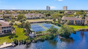 A residential area with a tennis court, a body of water, and surrounding greenery. - Waterfront Condo, 8 min drive to Marco Beaches (Naples)