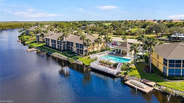 A residential area with a large swimming pool surrounded by houses and a river. - Waterfront Condo, 8 min drive to Marco Beaches (Naples)