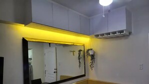 Une salle de bain avec un grand miroir, des toilettes et un lavabo. On aperçoit une porte blanche au fond, et une petite plante est accrochée au mur.