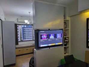 A modern living room with a flat-screen TV mounted on a wall, a built-in bench along the window, and a small shelf with decorative items.