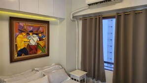 Une chambre d’hôtel avec un lit, une petite table de chevet, un tableau au mur et une fenêtre avec des rideaux.